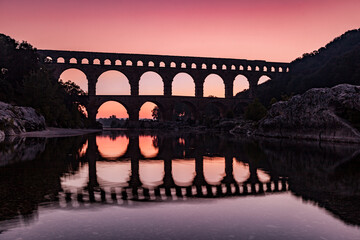 Pont du Gard, ancient Roman aqueduct bridge, sunrise, silhouette of arches and colorful red sky, Gorges du Gardon, natural landscape designated Biosphere Reserve by UNESCO, Provence, France