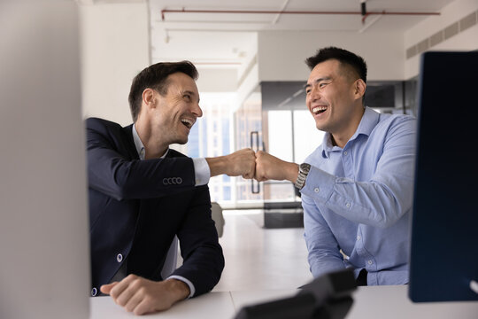 Two happy diverse financial traders making fist bump gesture, celebrating profit, income, professional win, successful deal on stock market, achievement, smiling, laughing, enjoying teamwork result