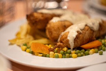 Traditional Montenegrin dish Podgorički popeci - meat rolls stuffed with ham and cheese, on white plate with peas, corn and french fries.