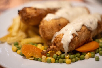 Traditional Montenegrin dish Podgorički popeci - meat rolls stuffed with ham and cheese, on white plate with peas, corn and french fries.