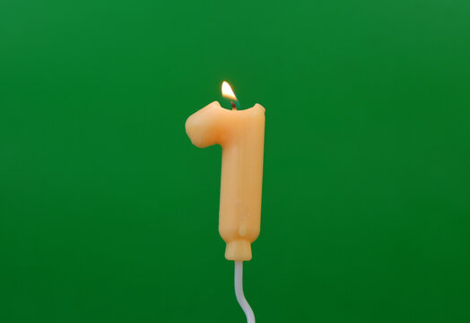 Air balloon shaped birthday candle burning on green background. Number 1.