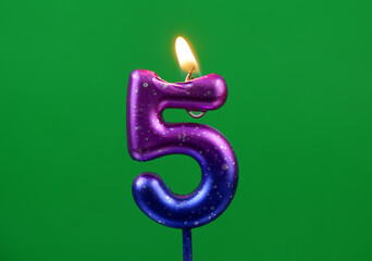Burning pink and blue birthday candle on green background, number 5