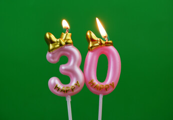 Burning pink birthday candles with golden bow and word happy on green background, number 30.