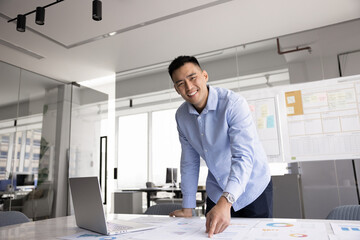 Happy successful Asian business leader man posing at large workplace table, working on project...