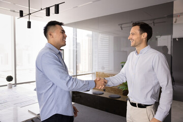 Happy male multiethnic business partners shaking hands in office after meeting, negotiation,...