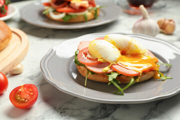 Tasty brunch. Poached egg, ham, tomato, arugula and bun on white marble table, closeup