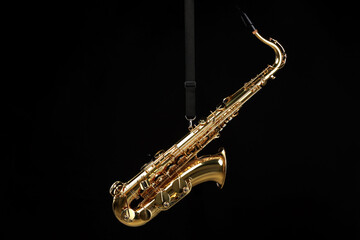 Jazz. One beautiful saxophone hanging from strap on black background