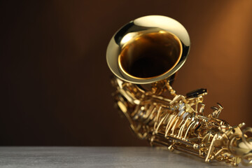 Jazz. One beautiful saxophone on light grey table against brown background, closeup. Space for text