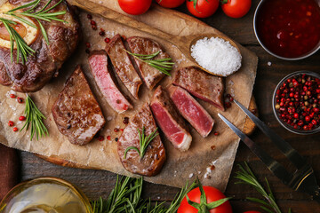 Pieces of delicious beef meat, spices and tomatoes on wooden table, flat lay