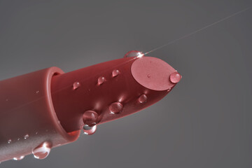 Classic lipstick with drops of water on a neutral background.