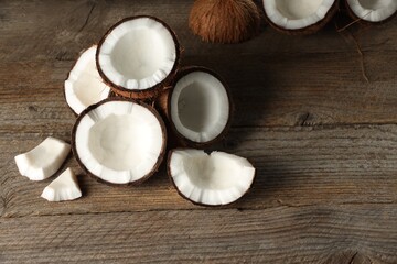 Pieces of cracked coconuts on wooden table, space for text