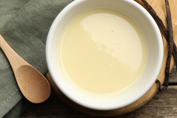 Tasty condensed milk, spoon and vanilla pods on wooden table, flat lay