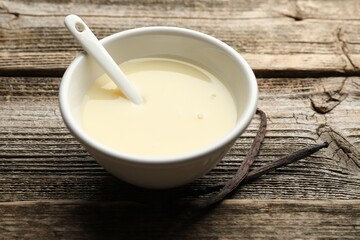 Tasty condensed milk, spoon and vanilla pods on wooden table, closeup