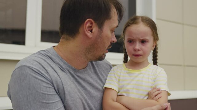 Caring father comforting his crying daughter, emotional moment between parent and child, little girl with teary eyes feeling sad, father supporting his upset daughter, family love and empathy, child