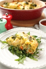 Tasty vegetable casserole and arugula on white table, closeup