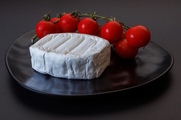 Soft brie cheese with fresh cherry tomatoes on a black plate