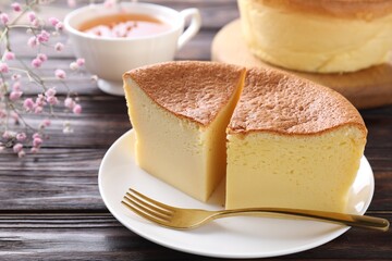 Pieces of tasty Japanese Castella sponge cake, tea, gypsophila flowers and fork on wooden table, closeup