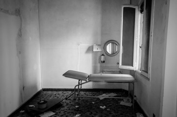 Una sala dell&rsquo;ospedale abbandonato del Lido di Venezia con una barella e un piccolo specchio rotondo illuminati dalla luce che entra da una finestra aperta