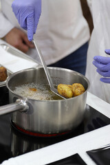 chef cocinando y friendo buñuelos de pescado en una olla en la cocina con sus guantes