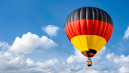 Fototapeta premium Colorful hot air balloon soaring through a clear blue sky with fluffy clouds above a scenic landscape