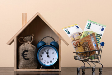 Symbolic wooden house and euro banknotes in a shopping cart