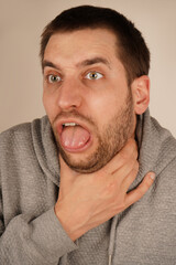 A man holds his throat with one hand, opening his mouth as if he is coughing or struggling to...