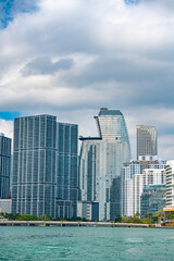 Obraz premium Cityscape by the Sea: A stunning cityscape of towering buildings by the ocean under a cloudy sky, capturing the harmony between architecture and nature.