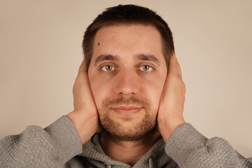 A European man covers his ears with his hands, trying to block out the loud noise. His face shows discomfort. This gesture communicates the frustration and stress he is experiencing.