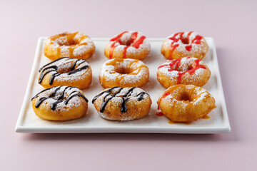 donuts with powdered sugar and various toppings on a white plate on a pale purple background. Top view . Copy space