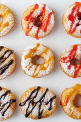 A group of donuts with powdered sugar and various toppings on a white plate close-up. Top view
