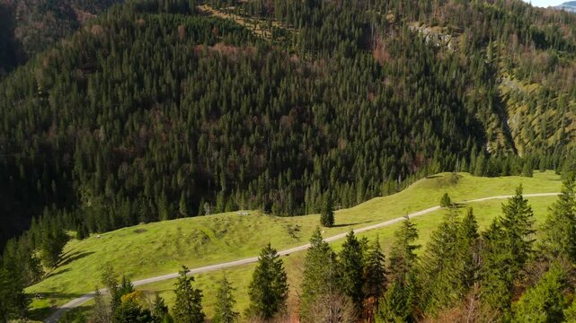 Aerial view of cyclist riding gravel bike through mountain valley in Bavaria, Germany near Valepp. Surrounded by alpine landscapes, rolling hills and autumn colors. Adventure, freedom and serenity. 