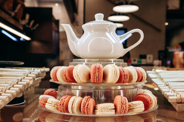 A display of delicious macarons with a teapot, arranged on a glass stand in a cafe setting