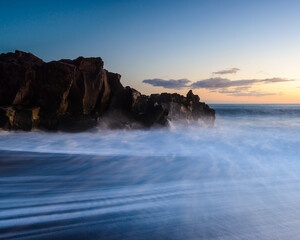Golden sunset over rocky coast with waves crashing on shore in Madeira
