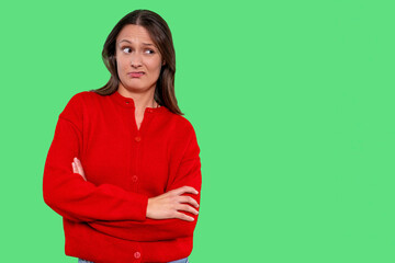 Woman with skeptical expression wearing a red sweater stands against a bright green background...