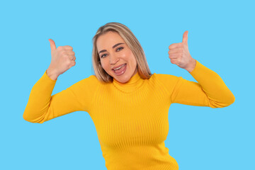 Smiling woman in yellow sweater giving thumbs up in front of bright blue background 