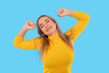 Fototapeta premium Joyful woman stretching in bright yellow sweater against blue background