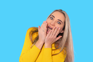 Excited young woman expressing surprise with hands on her face against a bright blue background...