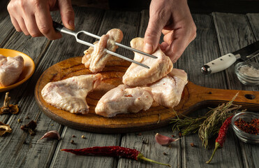 Hands carefully sort through raw chicken wings on a wooden cutting board. A knife, herbs and garlic are laid out nearby, indicating that a fragrant dish is being prepared