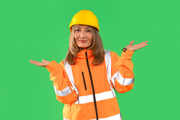 Construction worker wearing safety gear poses with a welcoming gesture against a green background