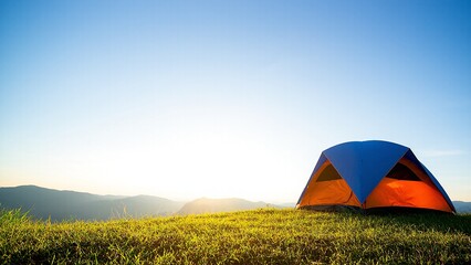 Camping tent on a grassy hilltop with mountains in the background against a clear blue sky.