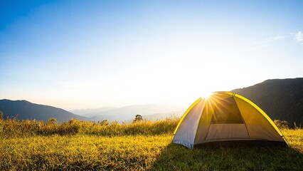 Sunrise camping: A yellow tent glows amidst grassy hills, with mountains fading into the distance under a clear blue sky.