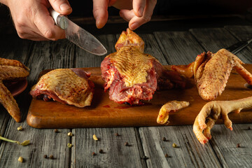 A skilled chef carefully cuts fresh poultry on a wooden cutting board, surrounded by various chicken parts, in a warm and rustic kitchen setting