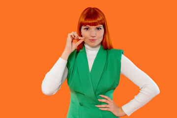 Stylish woman with red hair poses confidently keep mouth shut against a vibrant orange background...