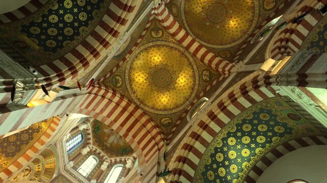 Magnificent golden mosaics and ornate arches decorate the ceiling inside Notre-Dame de la Garde Basilica in Marseille, France, showcasing stunning religious and historical architectural details.