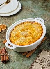 Finnish carrot casserole with rice and crispy crumble on top in white baking dish on green concrete background. Traditional food of Finns at Christmas. Vegetable, vegetarian recipes.