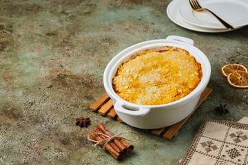 Finnish carrot casserole with rice and crispy crumble on top in white baking dish on green concrete background. Traditional food of Finns at Christmas. Vegetable, vegetarian recipes.