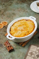 Finnish carrot casserole with rice and crispy crumble on top in white baking dish on green concrete background. Traditional food of Finns at Christmas. Vegetable, vegetarian recipes.
