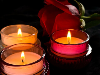 Two lit candles with a red rose on a dark background, creating a warm, romantic mood