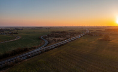 Aerial view of a highway cutting through vast rural fields under a golden sunset. The warm light...