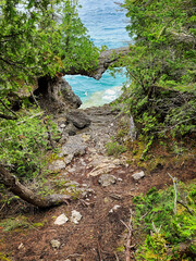 The view through a natural rocky heart-shaped arch overhang to blue and turquoise waters. Green shrubs on the rocks.